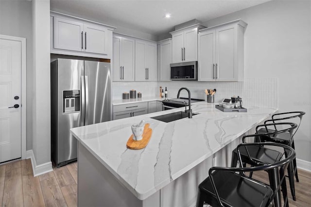 kitchen with a kitchen breakfast bar, light stone countertops, kitchen peninsula, and appliances with stainless steel finishes