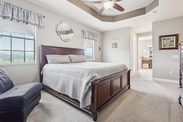 bedroom with ceiling fan, light carpet, ensuite bath, and a tray ceiling