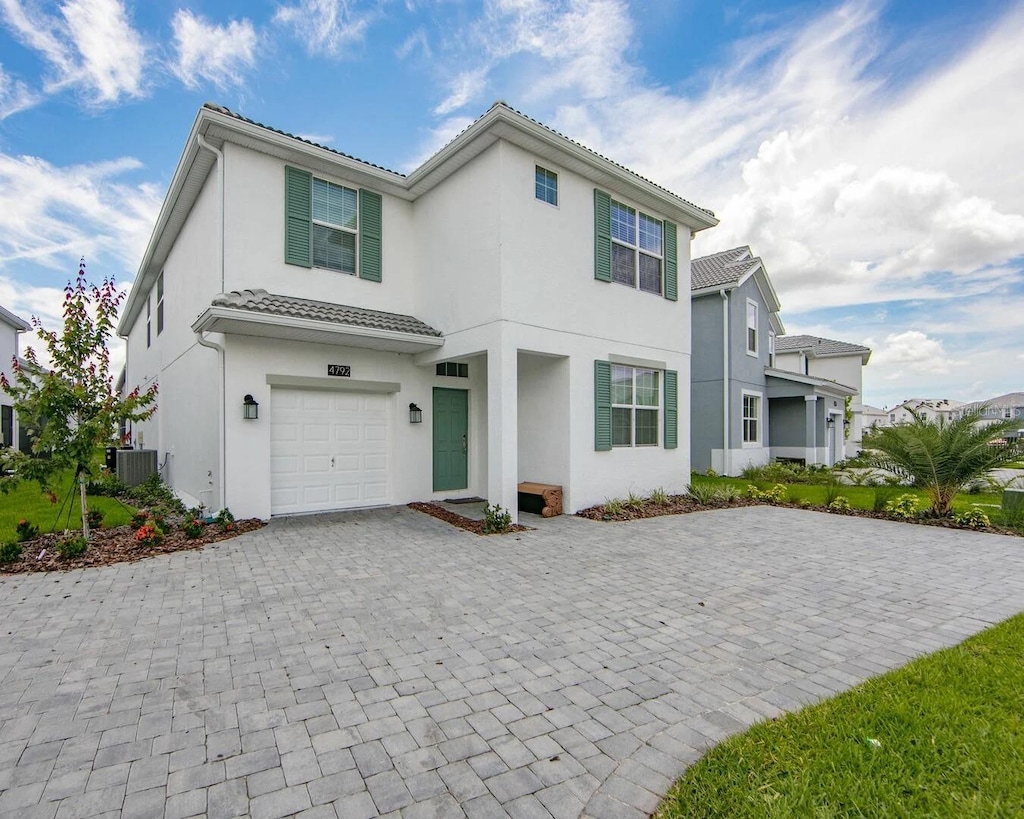 view of front of home with a tiled roof, an attached garage, cooling unit, decorative driveway, and stucco siding