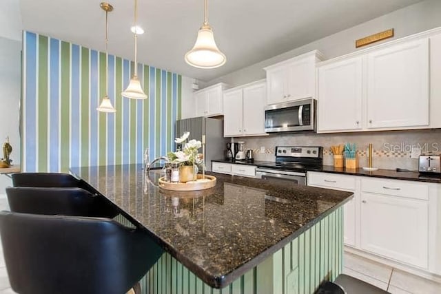 kitchen featuring stainless steel appliances, an island with sink, white cabinets, backsplash, and light tile floors