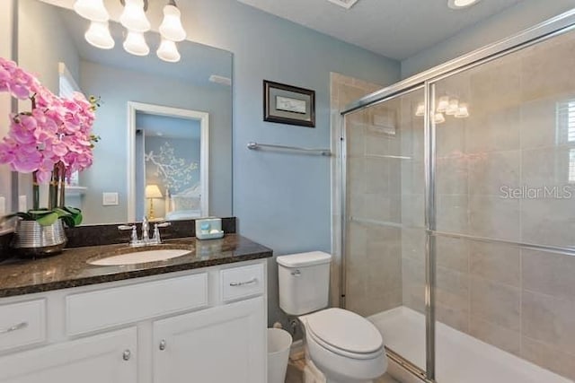 bathroom featuring an inviting chandelier, vanity with extensive cabinet space, toilet, and a shower with door