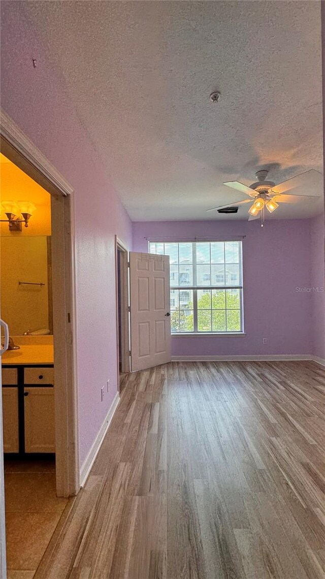 unfurnished living room with ceiling fan, a textured ceiling, and light hardwood / wood-style flooring