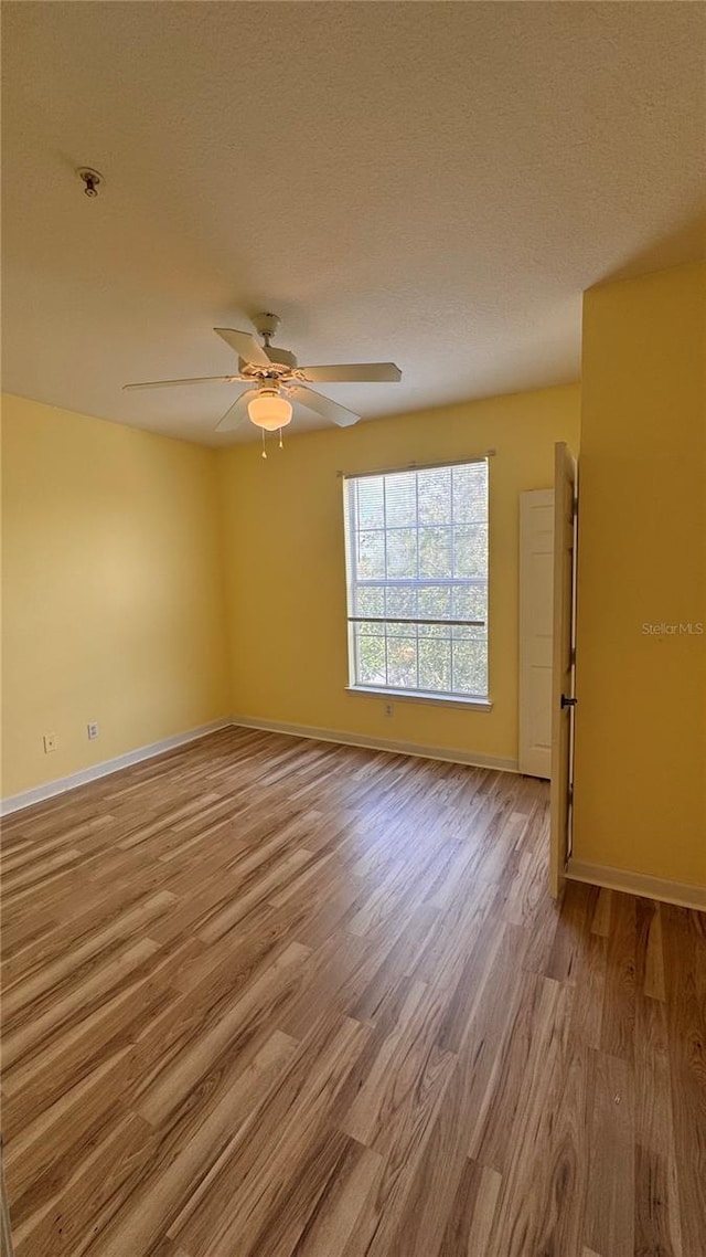 spare room featuring ceiling fan, light wood-type flooring, and a textured ceiling