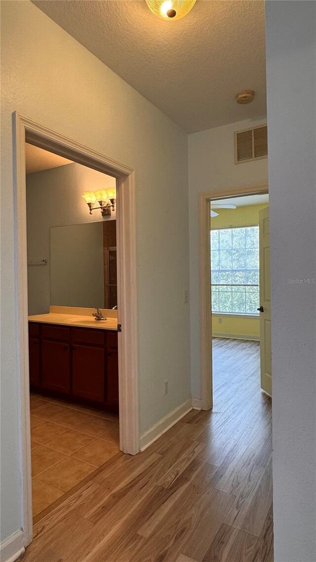 hall featuring sink, a textured ceiling, and light wood-type flooring