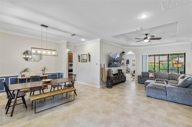 dining room with ceiling fan, a textured ceiling, a tray ceiling, and crown molding