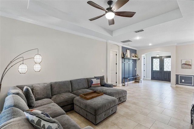 tiled living room with ceiling fan, ornamental molding, a tray ceiling, and french doors