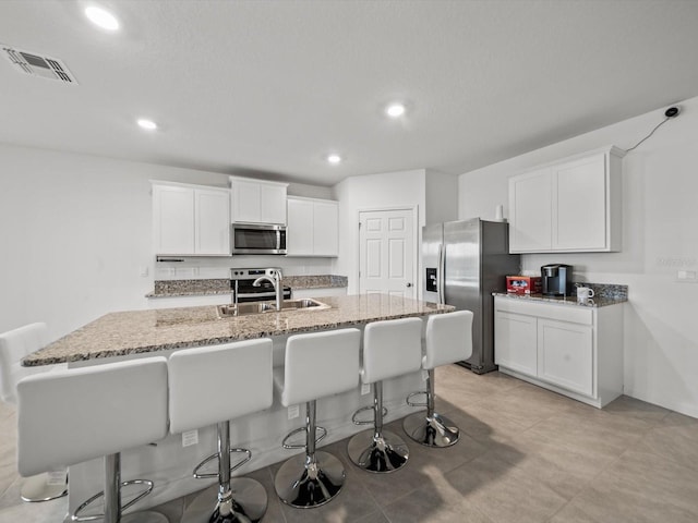 kitchen featuring sink, stainless steel appliances, a kitchen breakfast bar, a center island with sink, and white cabinets