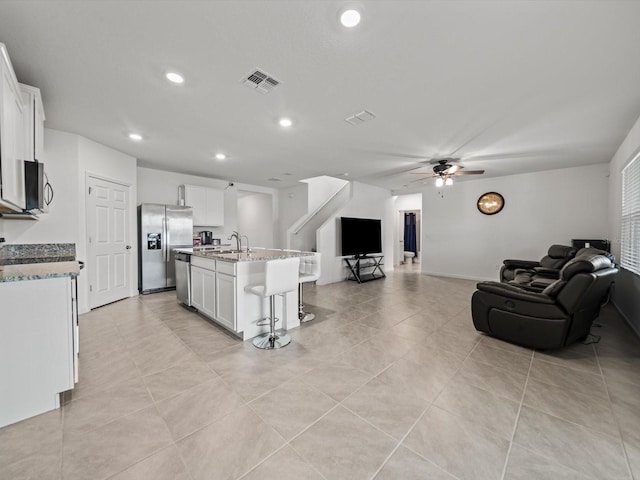 kitchen featuring light stone countertops, stainless steel appliances, a center island with sink, white cabinets, and a breakfast bar area