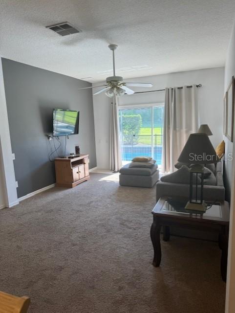 carpeted living area featuring baseboards, ceiling fan, visible vents, and a textured ceiling