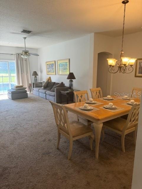 carpeted dining area featuring a textured ceiling, arched walkways, visible vents, and an inviting chandelier