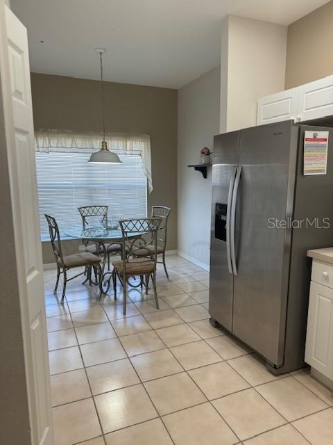 kitchen featuring stainless steel fridge with ice dispenser, light tile patterned flooring, white cabinets, and hanging light fixtures