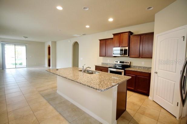 kitchen featuring sink, an island with sink, appliances with stainless steel finishes, light tile patterned flooring, and light stone counters