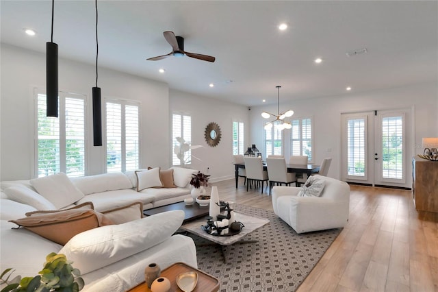 living room with ceiling fan with notable chandelier, french doors, light wood-type flooring, and plenty of natural light