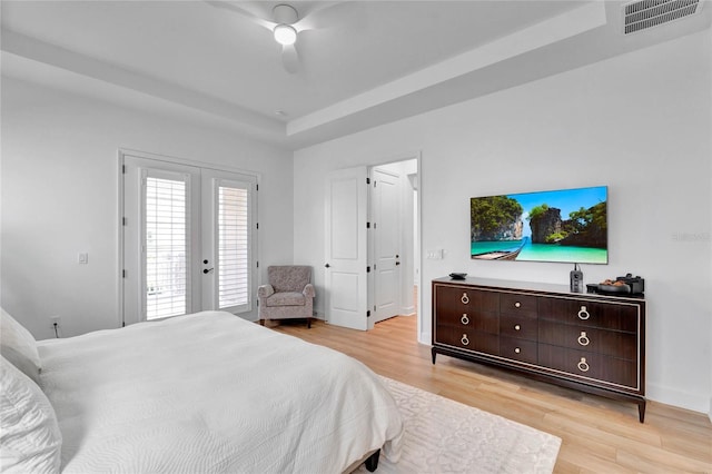 bedroom featuring french doors, access to outside, a tray ceiling, ceiling fan, and light hardwood / wood-style floors