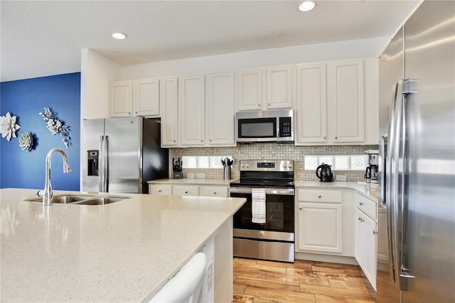 kitchen featuring sink, stainless steel appliances, tasteful backsplash, light stone counters, and white cabinets