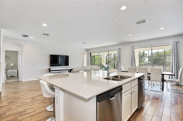 kitchen with dishwasher, sink, an island with sink, white cabinetry, and brick wall