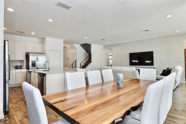 dining room with light wood-type flooring, a textured ceiling, and brick wall