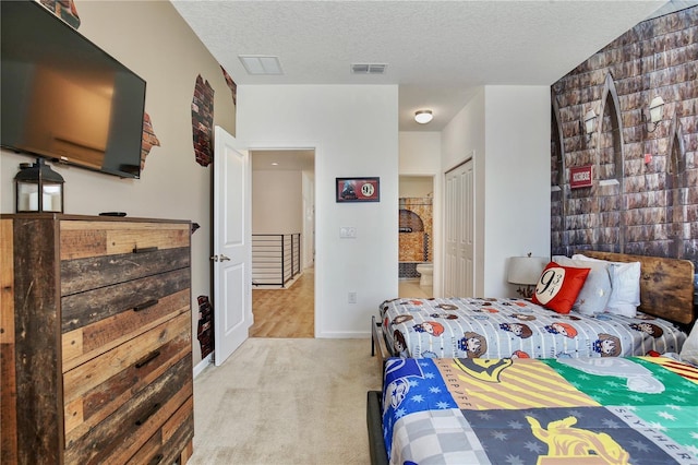 carpeted bedroom with a textured ceiling, ensuite bath, and a closet