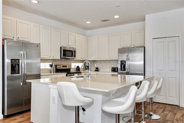 kitchen featuring a center island with sink, sink, appliances with stainless steel finishes, a kitchen bar, and white cabinetry