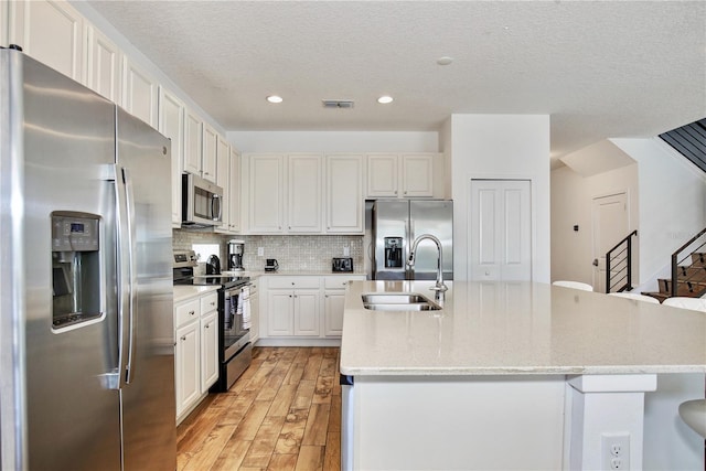 kitchen with tasteful backsplash, stainless steel appliances, sink, a center island with sink, and white cabinetry