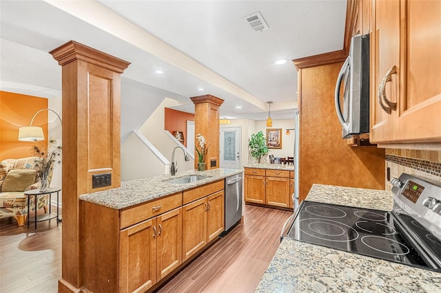 kitchen with brown cabinets, decorative columns, light wood-style flooring, appliances with stainless steel finishes, and a sink