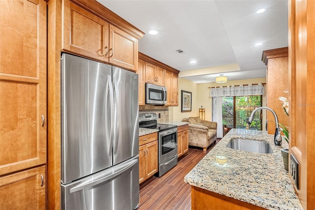 kitchen featuring dark wood-style flooring, backsplash, appliances with stainless steel finishes, a sink, and light stone countertops