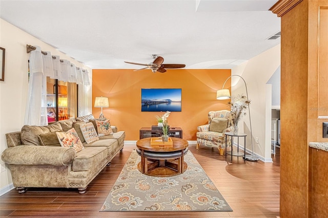 living area featuring baseboards, visible vents, dark wood finished floors, and a ceiling fan