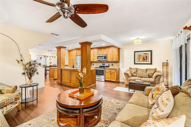 living area with decorative columns, baseboards, visible vents, ceiling fan, and dark wood-type flooring