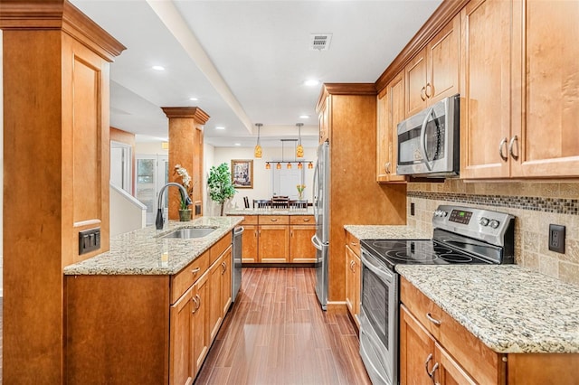 kitchen with decorative backsplash, appliances with stainless steel finishes, wood finished floors, light stone countertops, and a sink