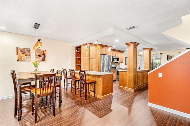 kitchen with brown cabinets, decorative columns, stainless steel appliances, visible vents, and a peninsula