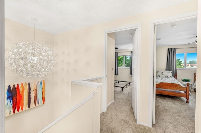 corridor featuring light colored carpet, plenty of natural light, a textured ceiling, and an inviting chandelier