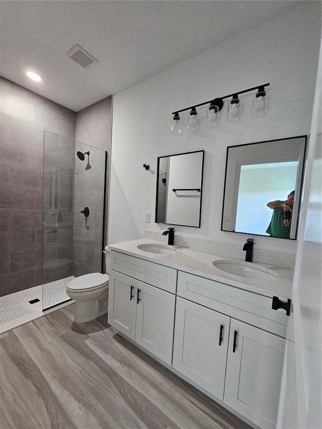 bathroom featuring hardwood / wood-style flooring, vanity, toilet, and a tile shower