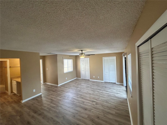 unfurnished bedroom with multiple closets, ceiling fan, hardwood / wood-style flooring, and a textured ceiling