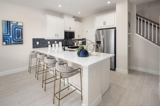 kitchen with sink, kitchen peninsula, stainless steel fridge, a breakfast bar area, and white cabinets