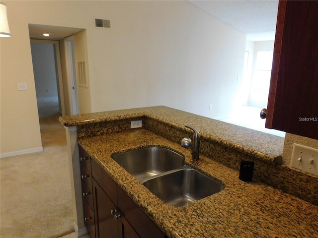 kitchen with dark stone countertops, sink, and light colored carpet