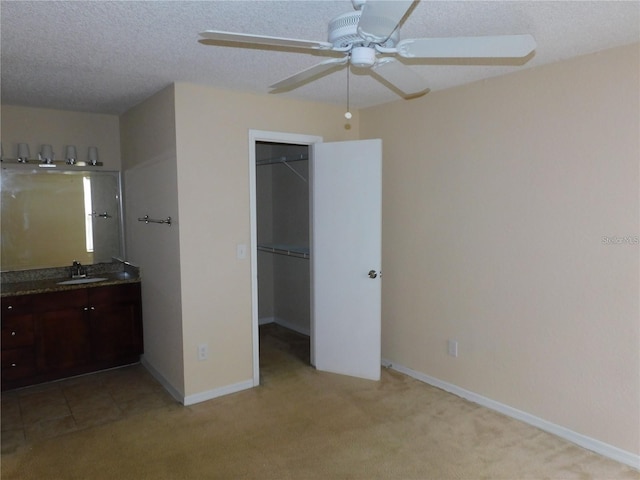 unfurnished bedroom with sink, a spacious closet, light colored carpet, and a textured ceiling