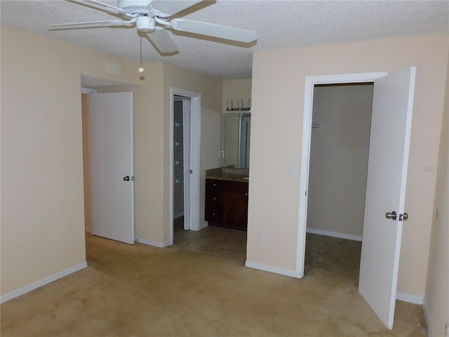 unfurnished bedroom featuring connected bathroom, a spacious closet, light colored carpet, a textured ceiling, and ceiling fan