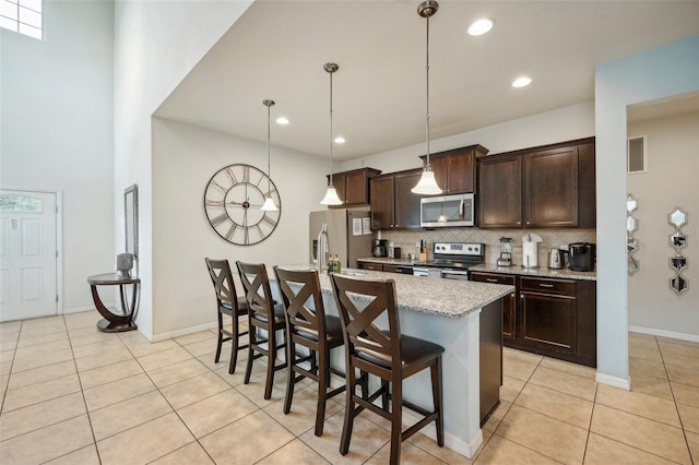 kitchen featuring a towering ceiling, tasteful backsplash, a kitchen bar, an island with sink, and appliances with stainless steel finishes