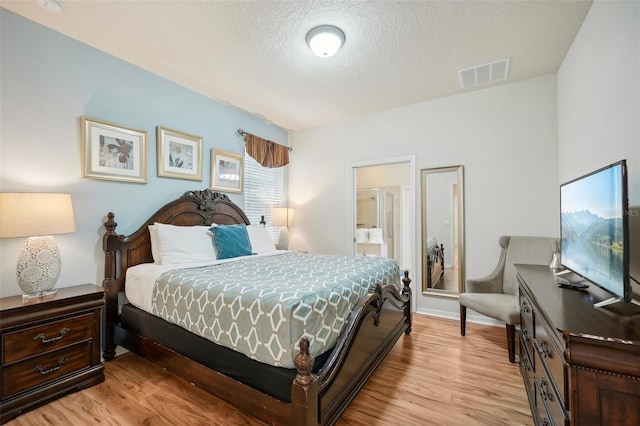 bedroom with ensuite bath, light hardwood / wood-style floors, and a textured ceiling