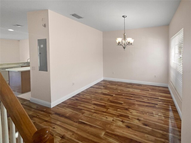 spare room featuring dark hardwood / wood-style flooring, electric panel, and an inviting chandelier