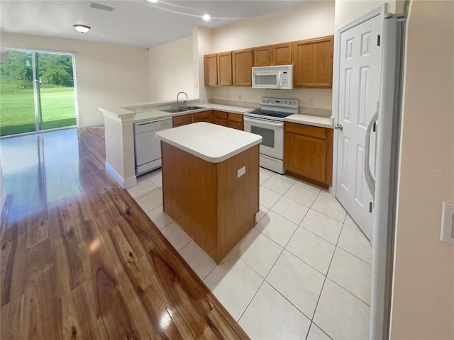 kitchen with kitchen peninsula, white appliances, sink, light tile patterned floors, and a center island