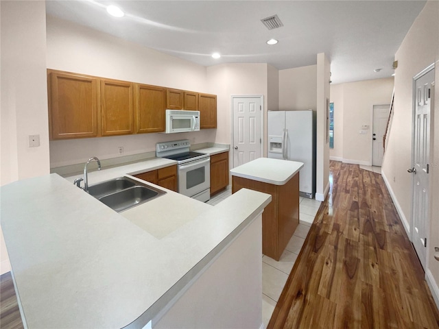 kitchen with hardwood / wood-style floors, a center island, white appliances, sink, and kitchen peninsula