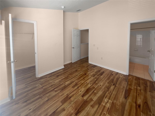 unfurnished bedroom with dark hardwood / wood-style floors, a spacious closet, ensuite bathroom, and a closet