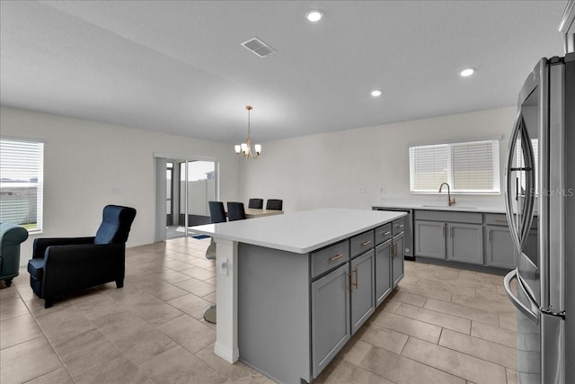 kitchen with a center island, stainless steel fridge, sink, light tile floors, and pendant lighting