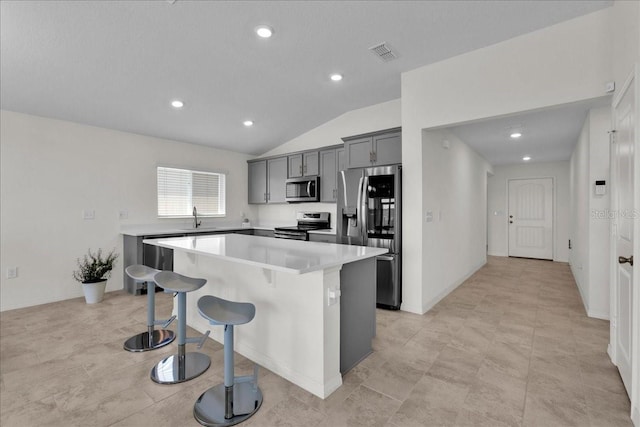 kitchen with a center island, lofted ceiling, gray cabinetry, appliances with stainless steel finishes, and a breakfast bar area