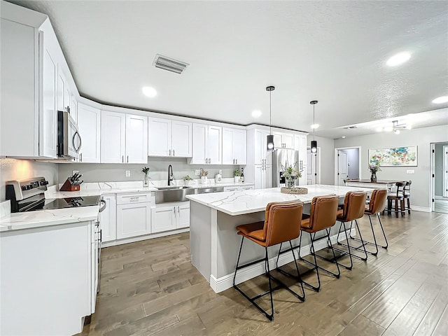 kitchen with appliances with stainless steel finishes, sink, decorative light fixtures, a center island, and white cabinetry