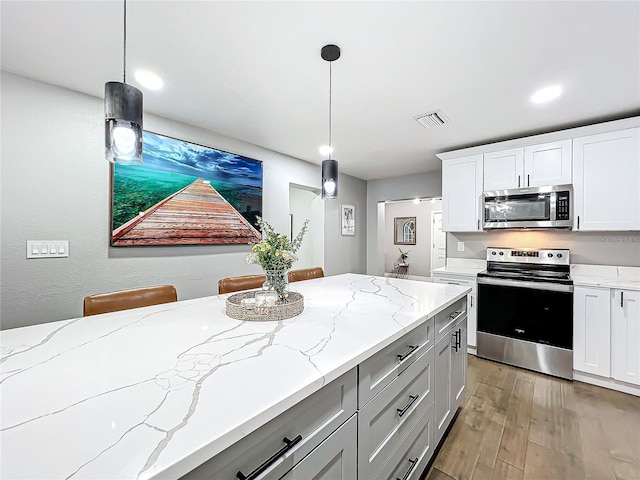 kitchen with appliances with stainless steel finishes, light wood-type flooring, light stone counters, pendant lighting, and white cabinetry