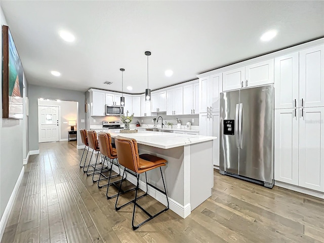 kitchen featuring a breakfast bar, a center island, white cabinets, appliances with stainless steel finishes, and decorative light fixtures