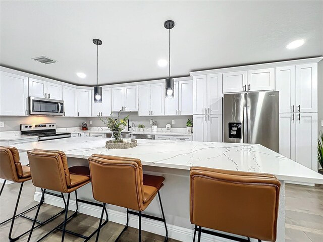 kitchen with white cabinets, a center island, hanging light fixtures, and appliances with stainless steel finishes