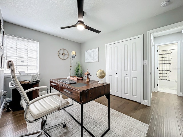 office area with a textured ceiling, ceiling fan, and dark wood-type flooring